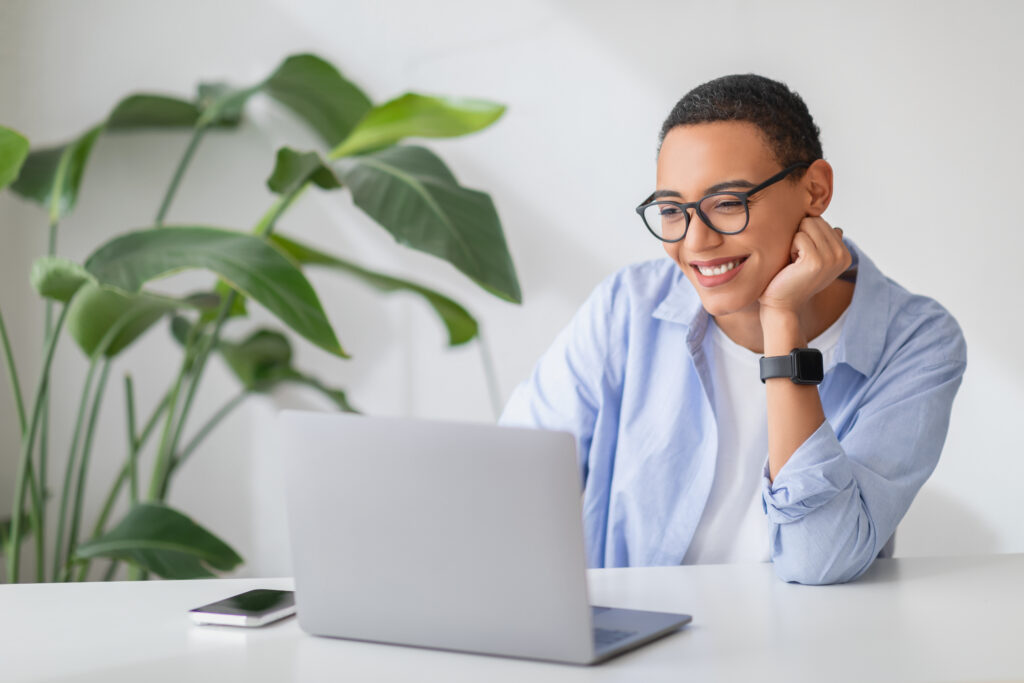 Cheerful young woman with glasses looking at her laptop screen, leaning on her hand Eye Services in Holly Springs, NC and Fayetteville, NC