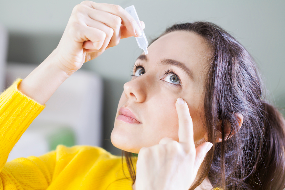 Young woman applying eye drops to help manage dry eye, in need of an eye evaluation.